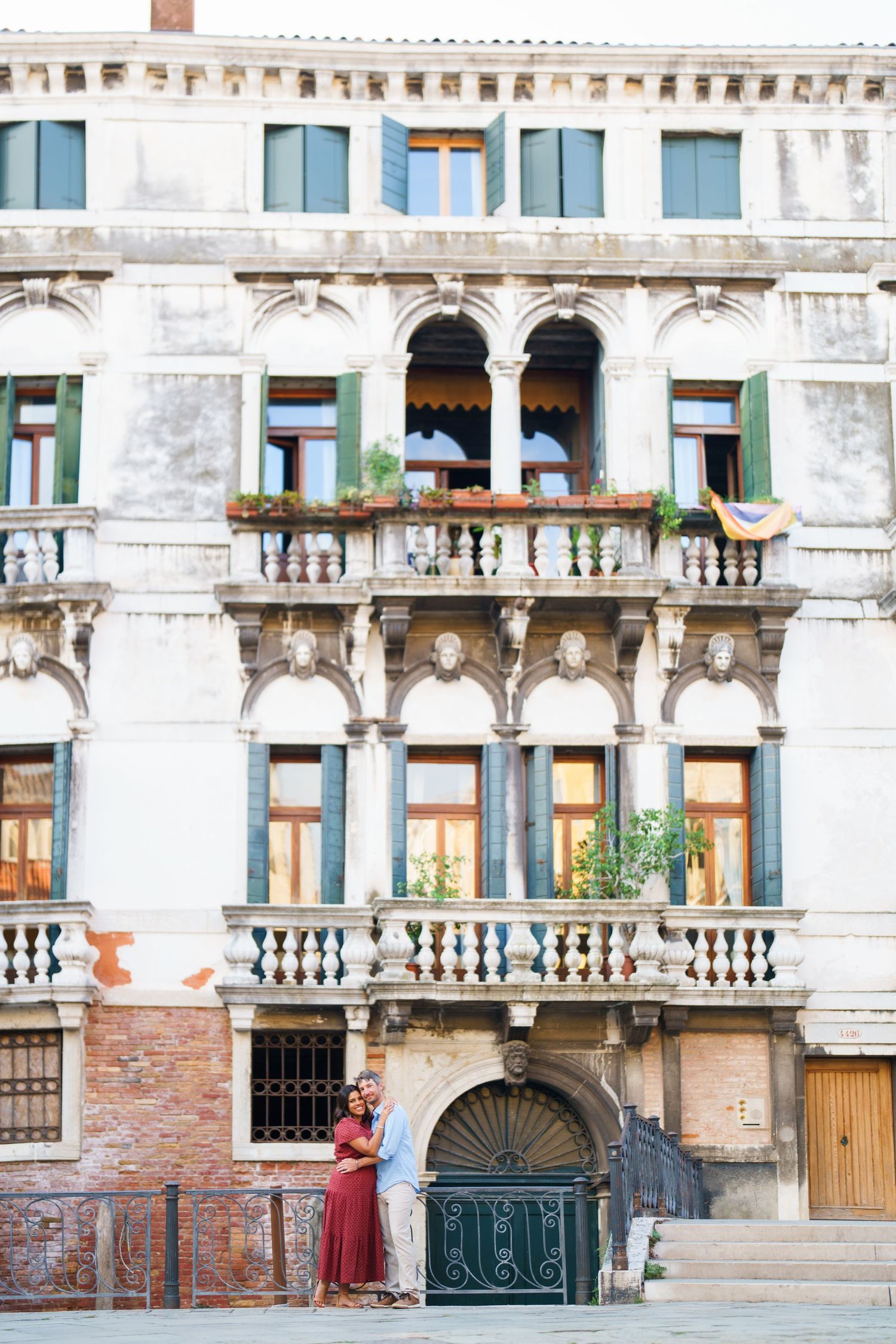 Couple embracing before ornate Venetian palace facade with arched windows and balconies in Venice, Italy.