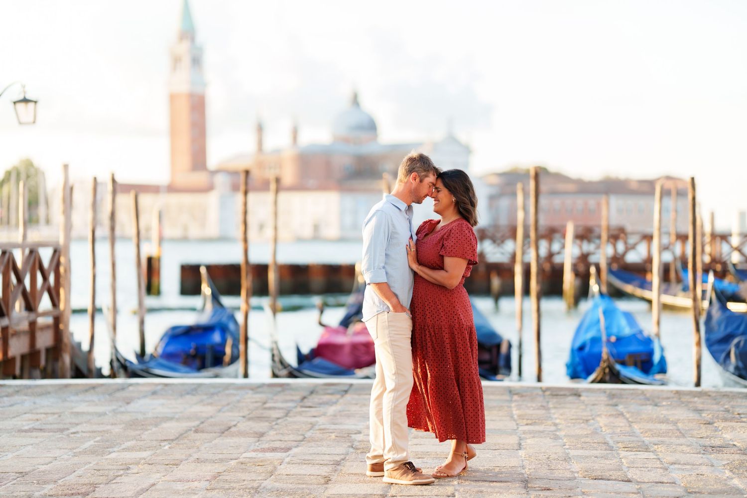 Romantic couple kissing by Venice gondolas with San Giorgio Maggiore church in background on sunny day.