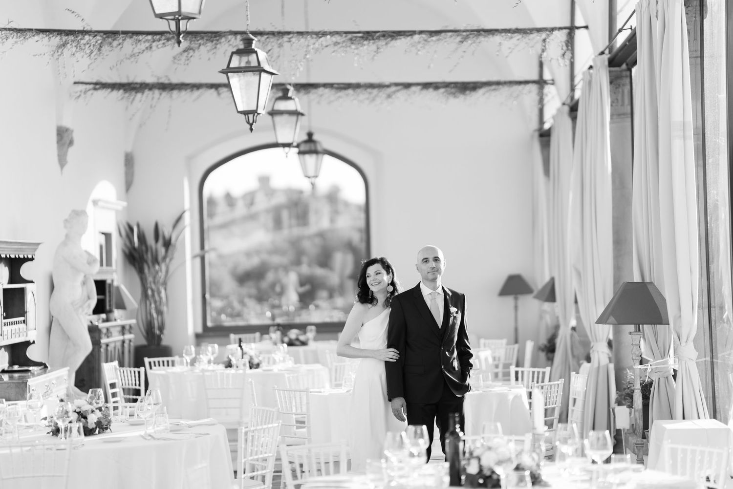 Black and white photo of elegant wedding reception hall with hanging chandeliers.