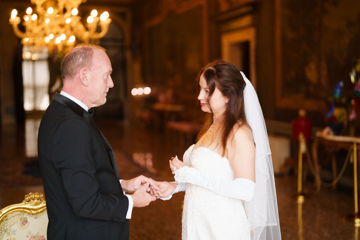 A wedding couple shares their first dance in an elegant ballroom under warm chandelier lighting.