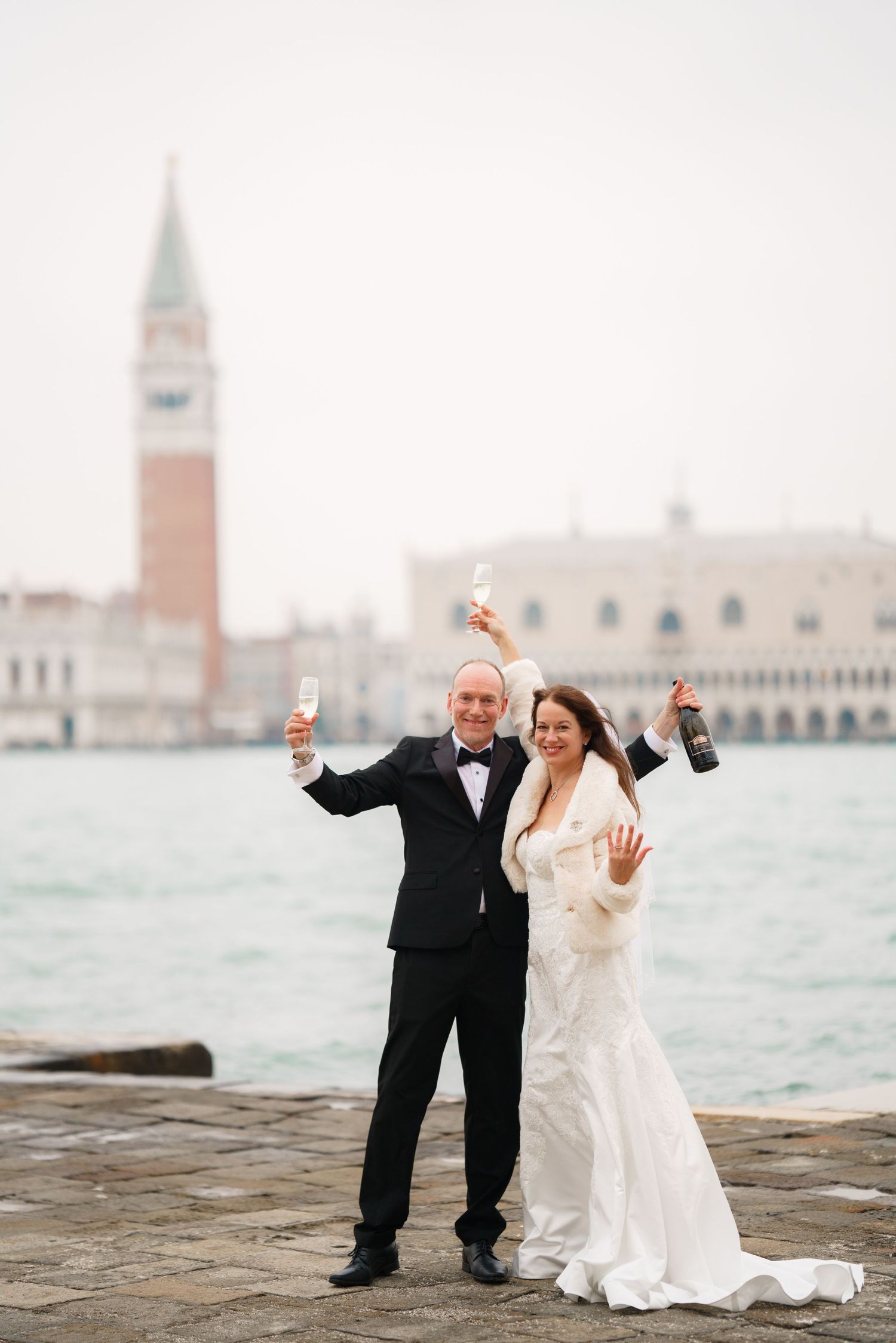 Couple celebrates their wedding by posing on the Venice waterfront with St. Mark's Campanile in the background.
