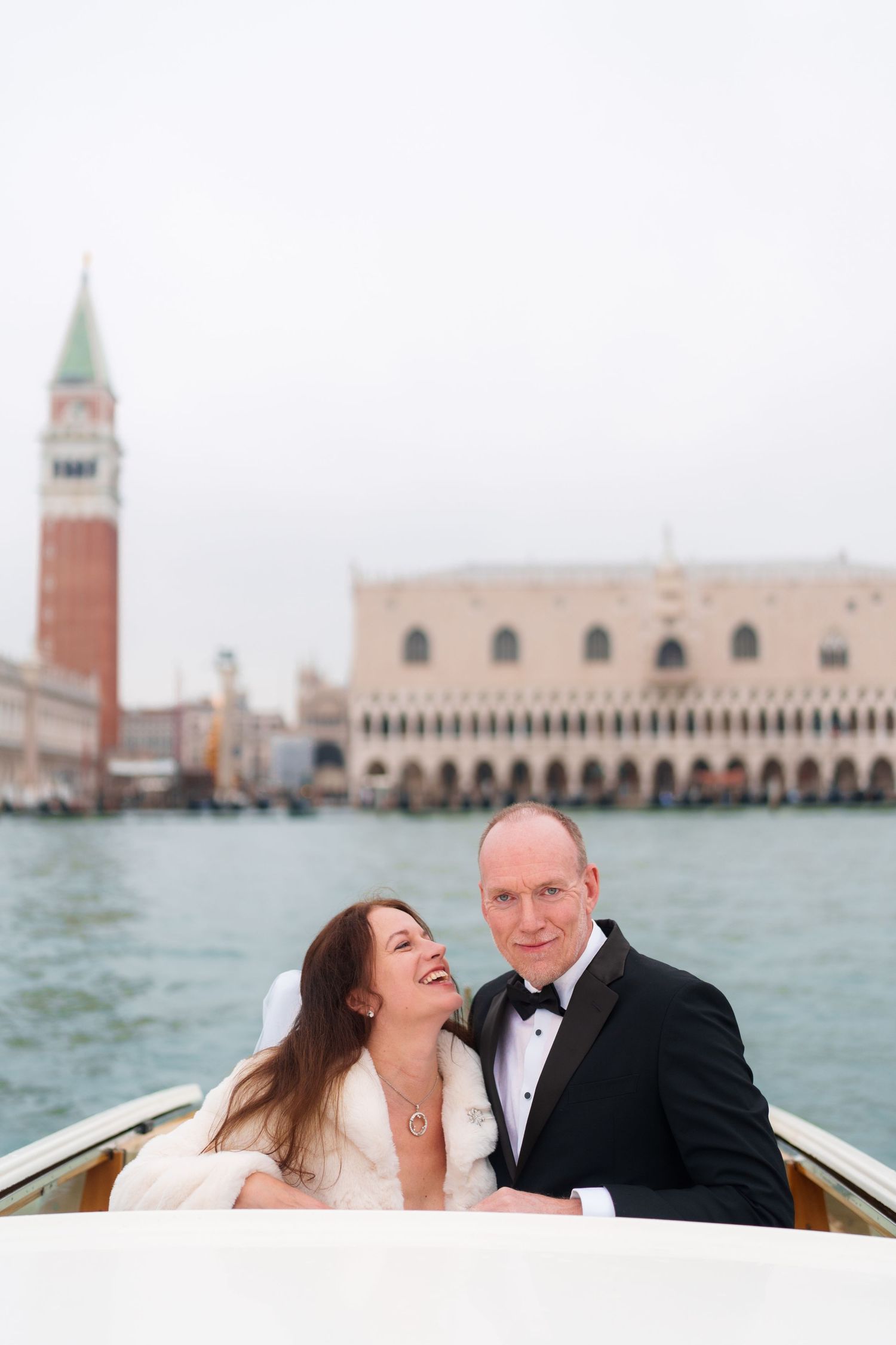 Couple enjoying romantic moments on a boat in Venice with the iconic St. Mark's Square and bell tower in background.
