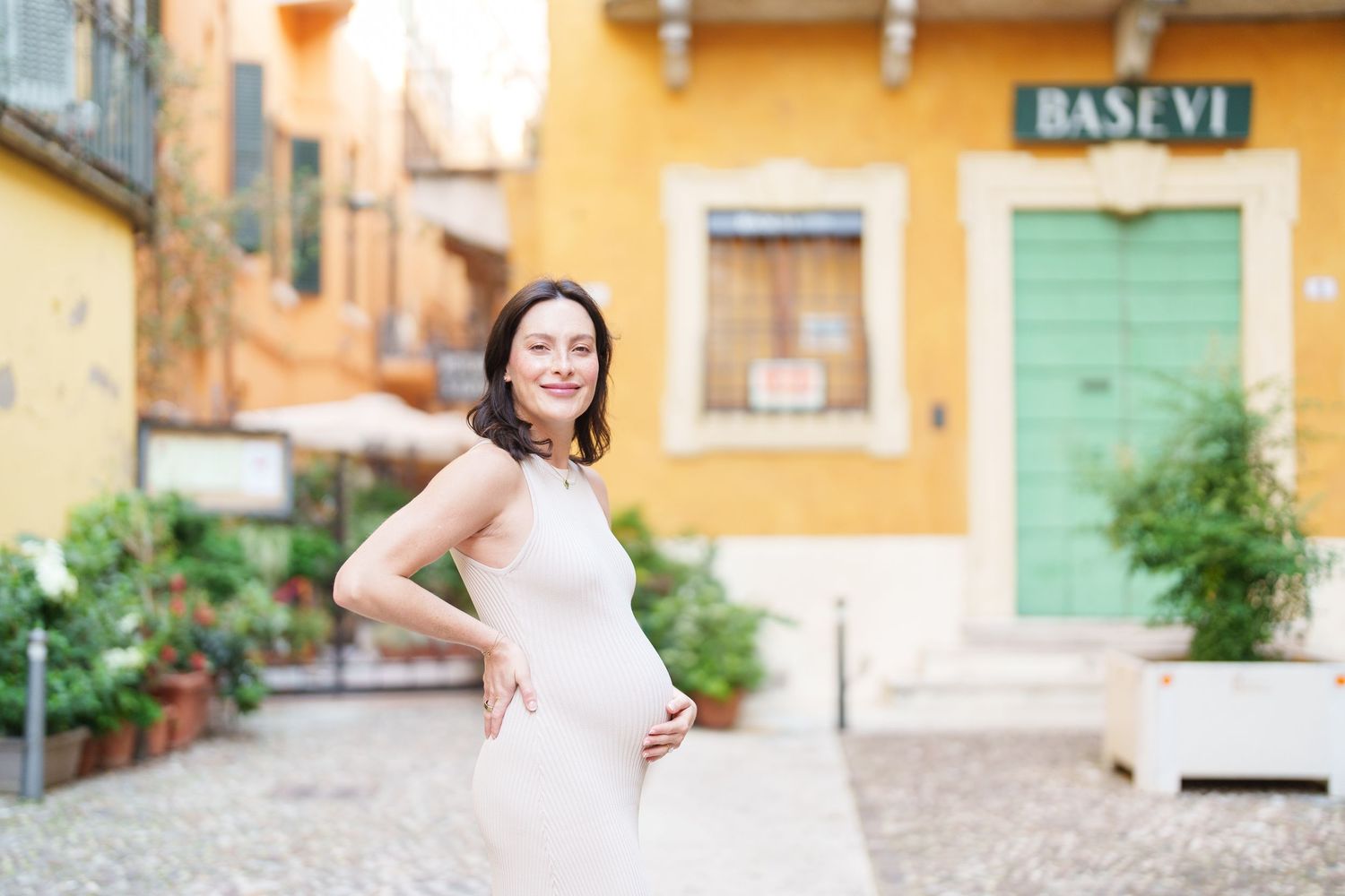 A bride in a white wedding dress poses in front of colorful buildings on a cobblestone street.