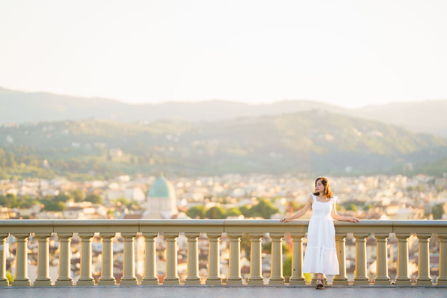 Panoramic view of a coastal city with mountains in the background and a white balustrade in the foreground.