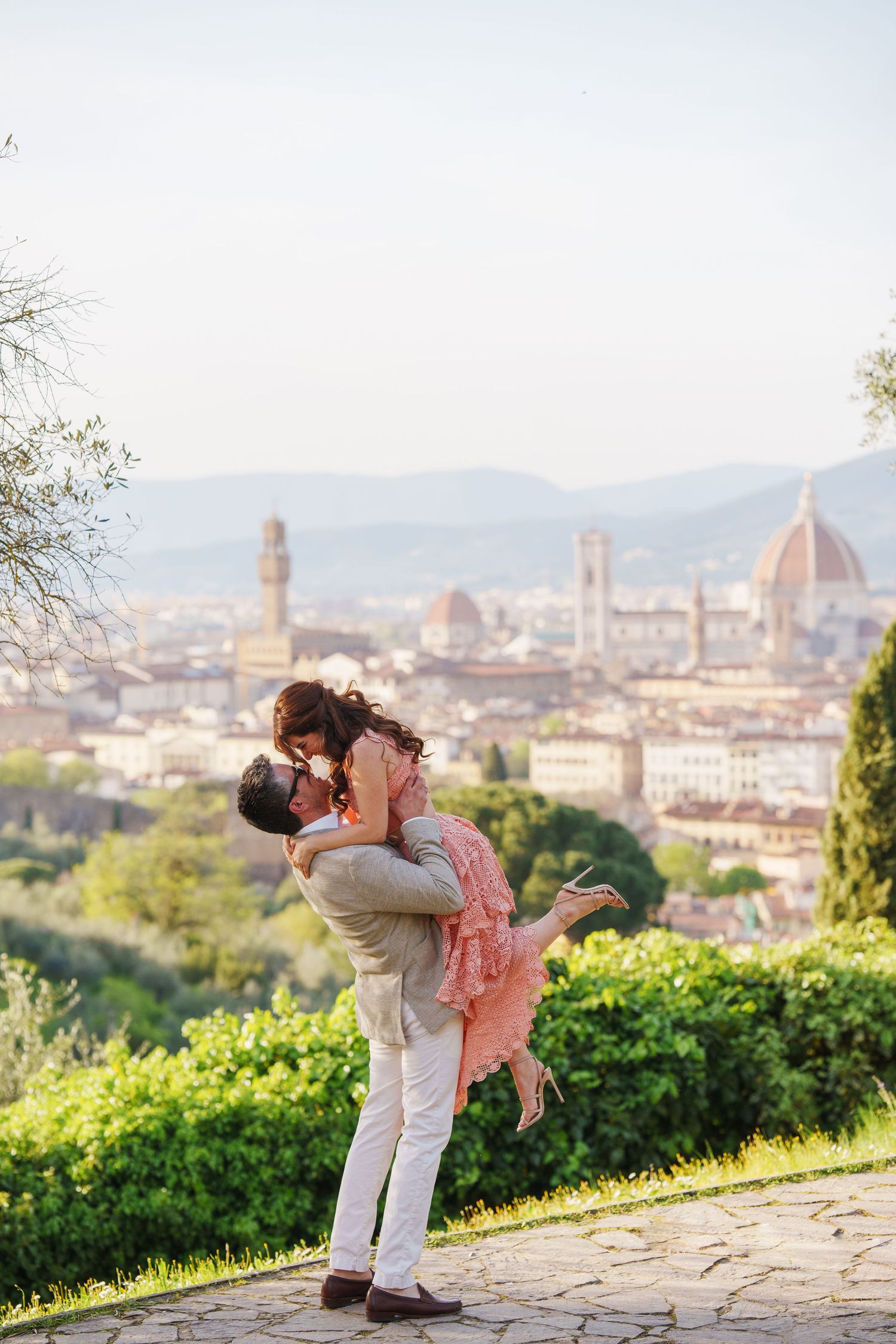 A romantic couple embraces against the stunning backdrop of Florence, Italy with the Duomo cathedral visible in the distance.