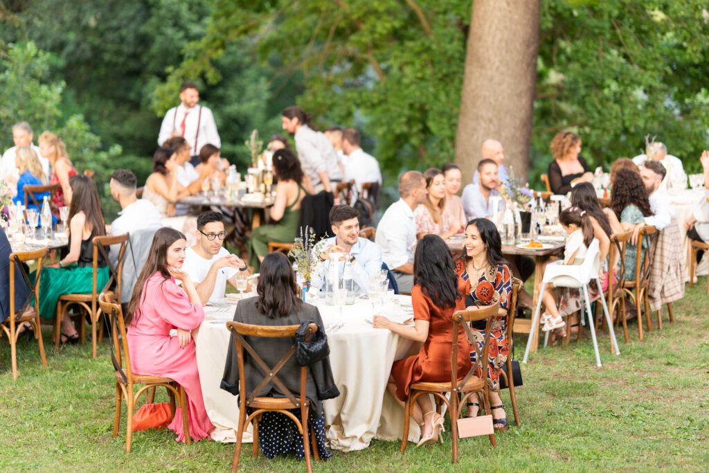 Outdoor wedding reception with guests seated at round tables under trees.
