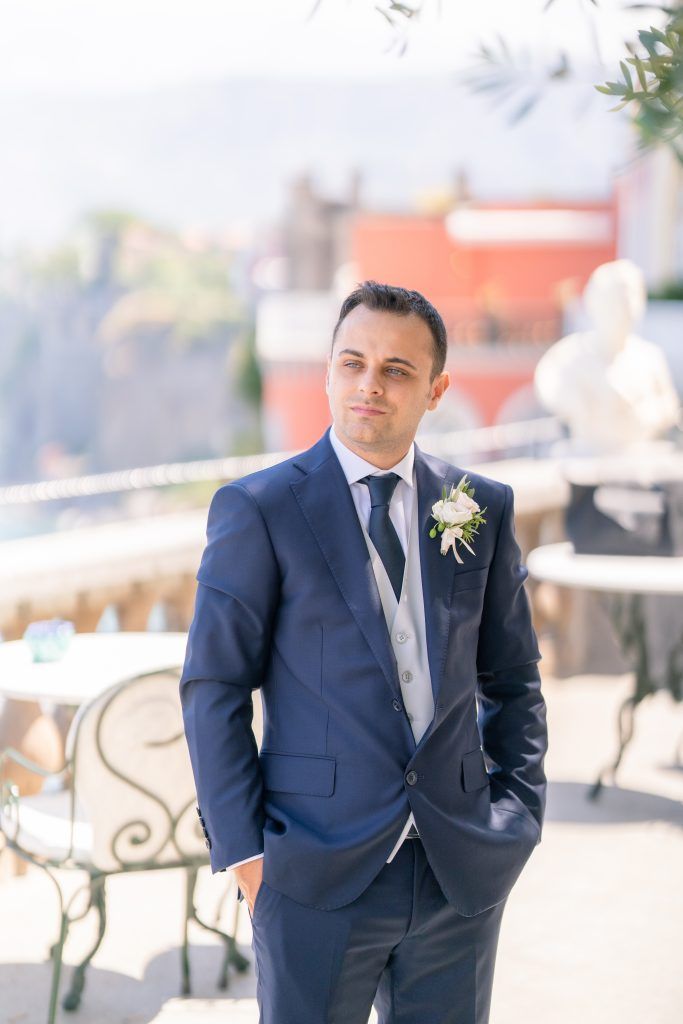 Groomsmen in navy suits and silver ties pose on a sunny outdoor terrace.