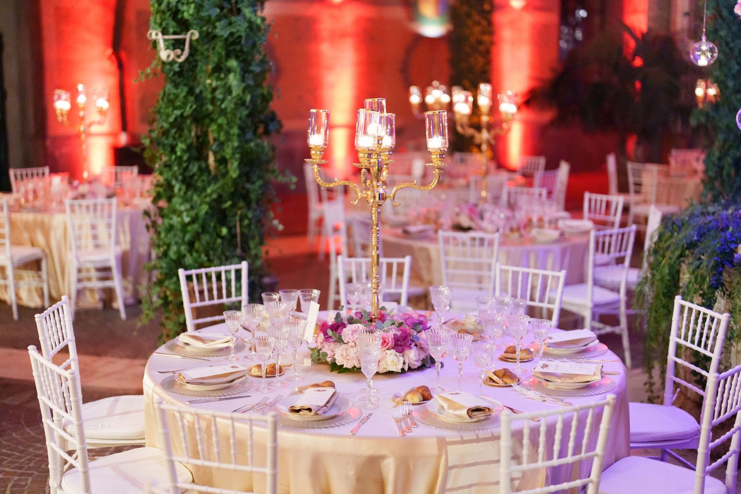 Wedding reception venue with dramatic red lighting and white Chiavari chairs.