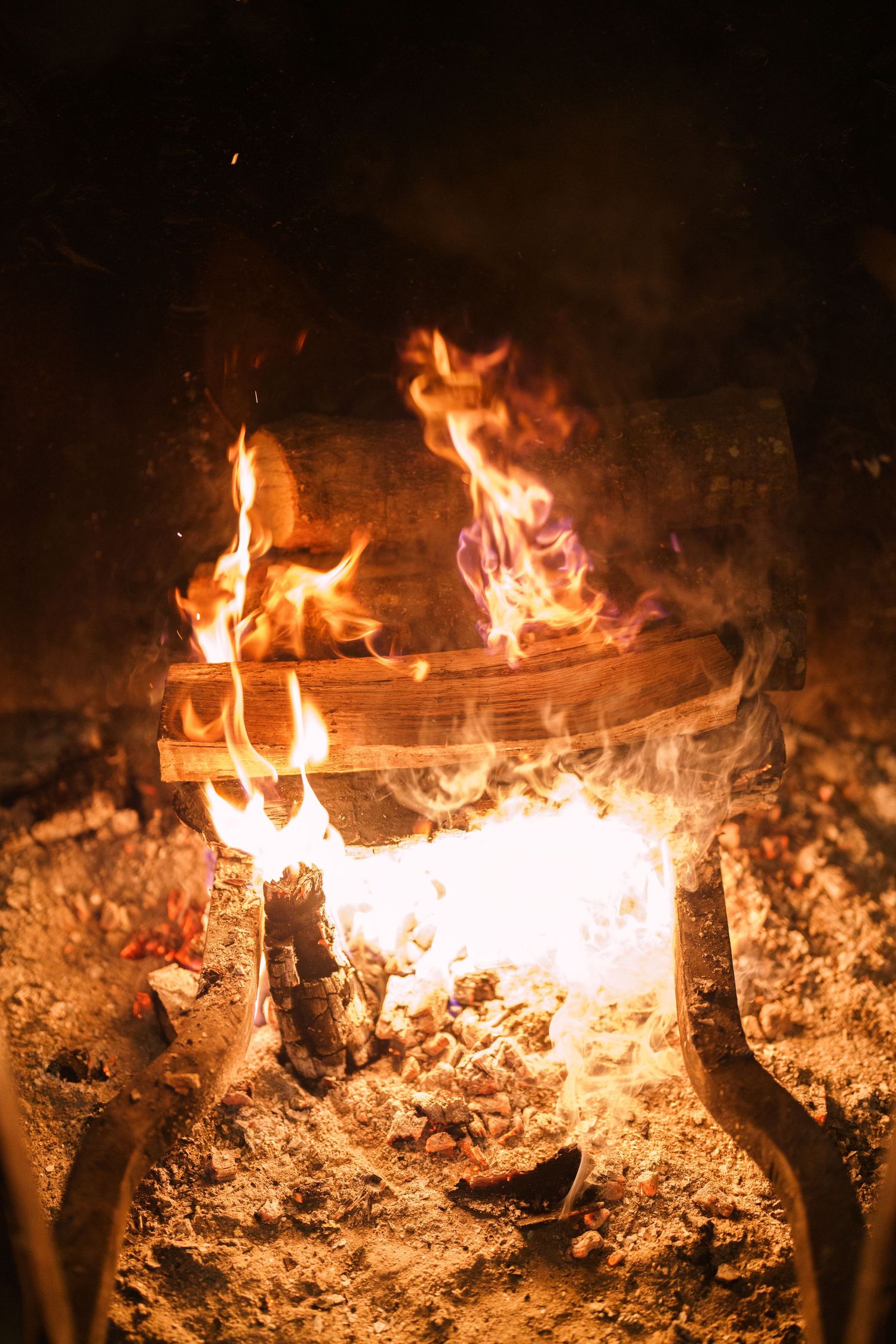 Burning logs and embers in a rustic fireplace create a warm, cozy atmosphere.