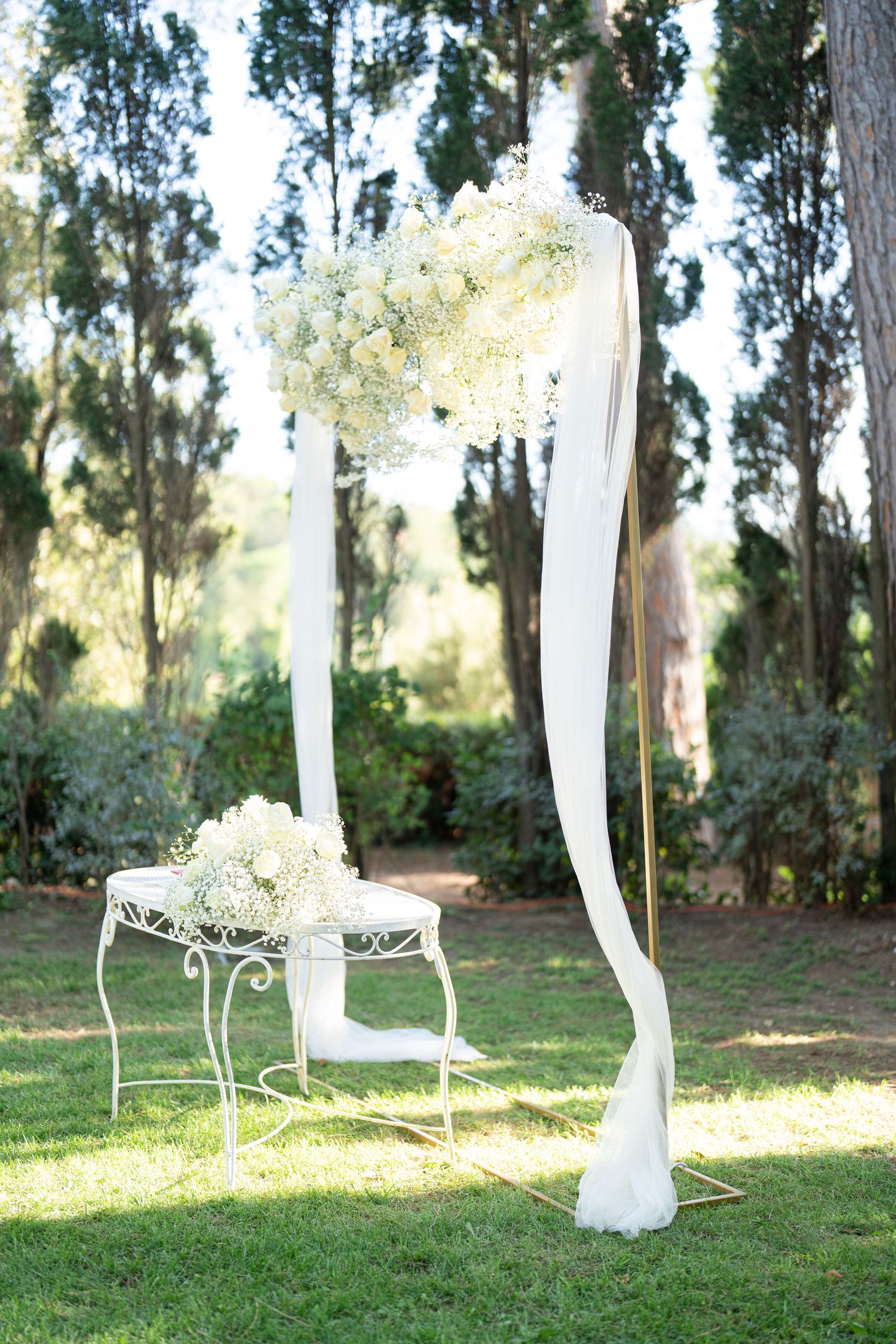White decorative chairs and flowing fabric drapes line a garden path for an outdoor wedding.