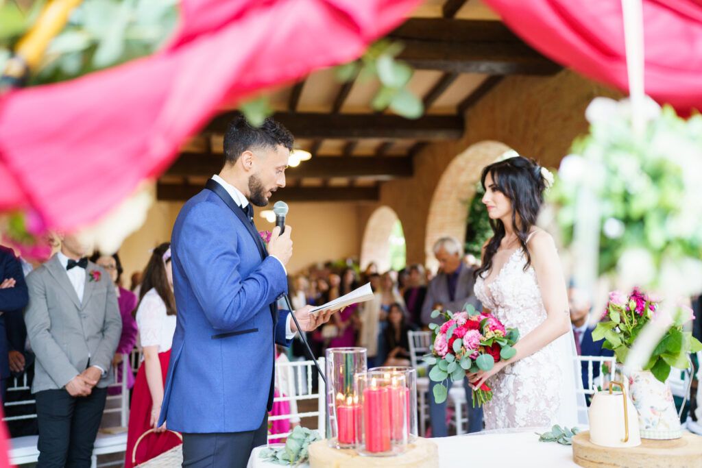 Wedding ceremony moment under covered venue with pink draping and floral decorations.