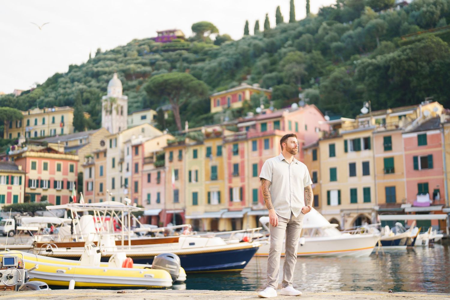 Colorful houses line the waterfront of Portofino Italy with boats moored in the Mediterranean harbor on a sunny day.