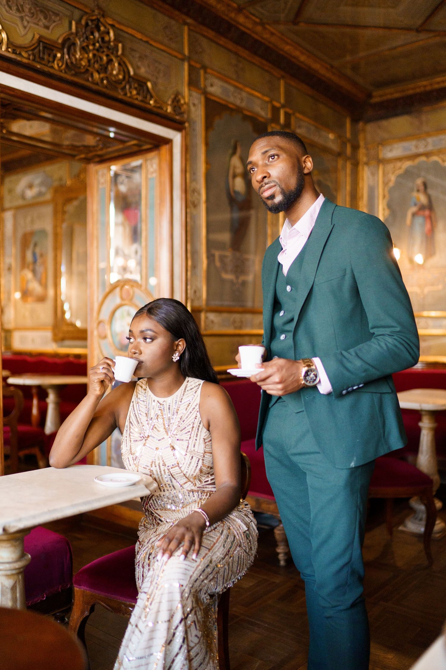 Couple shares romantic moment in elegant vintage room with ornate gold decor and plush red seating.