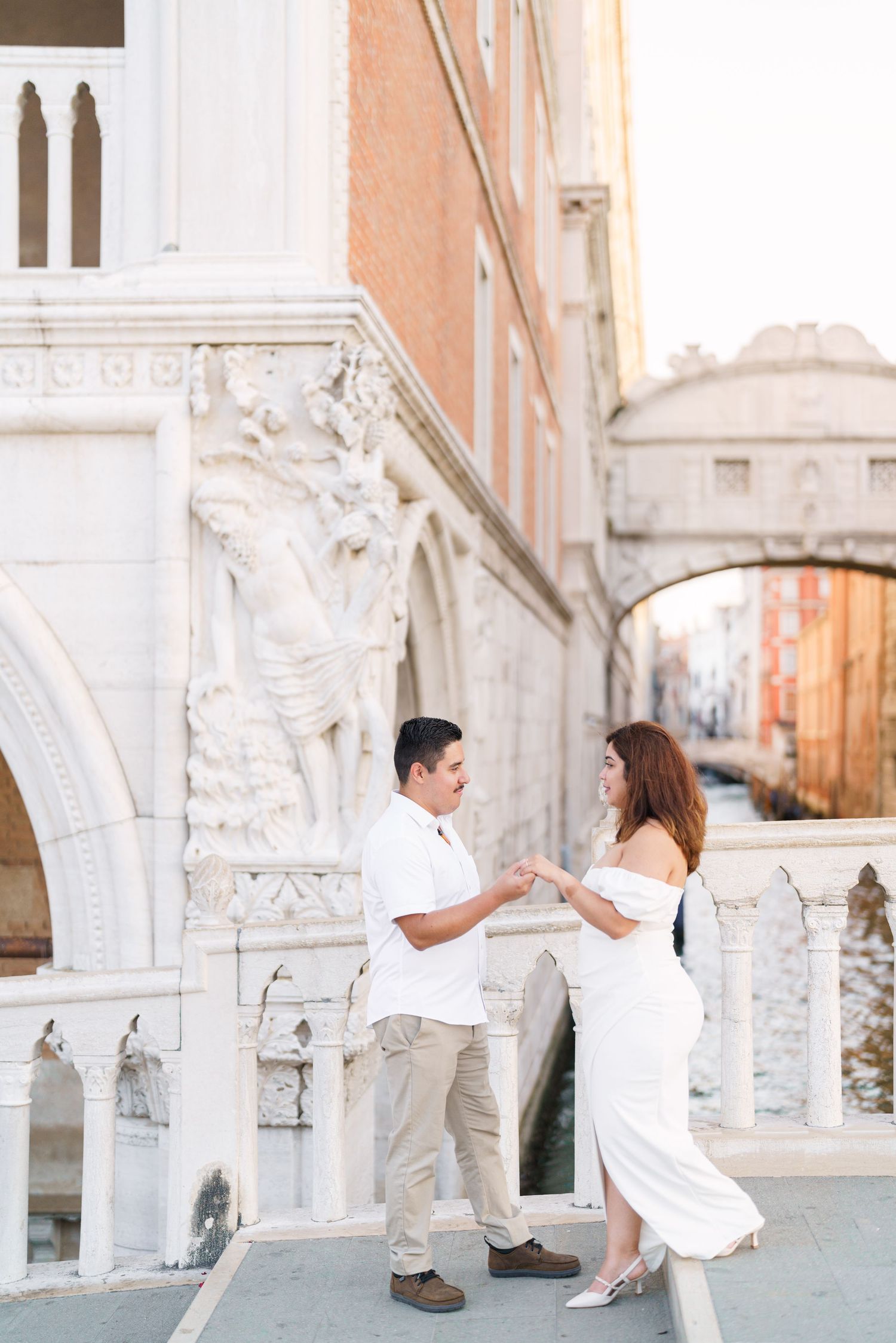 A couple shares romantic moments against ornate white stone architecture in Venice during a photo session.