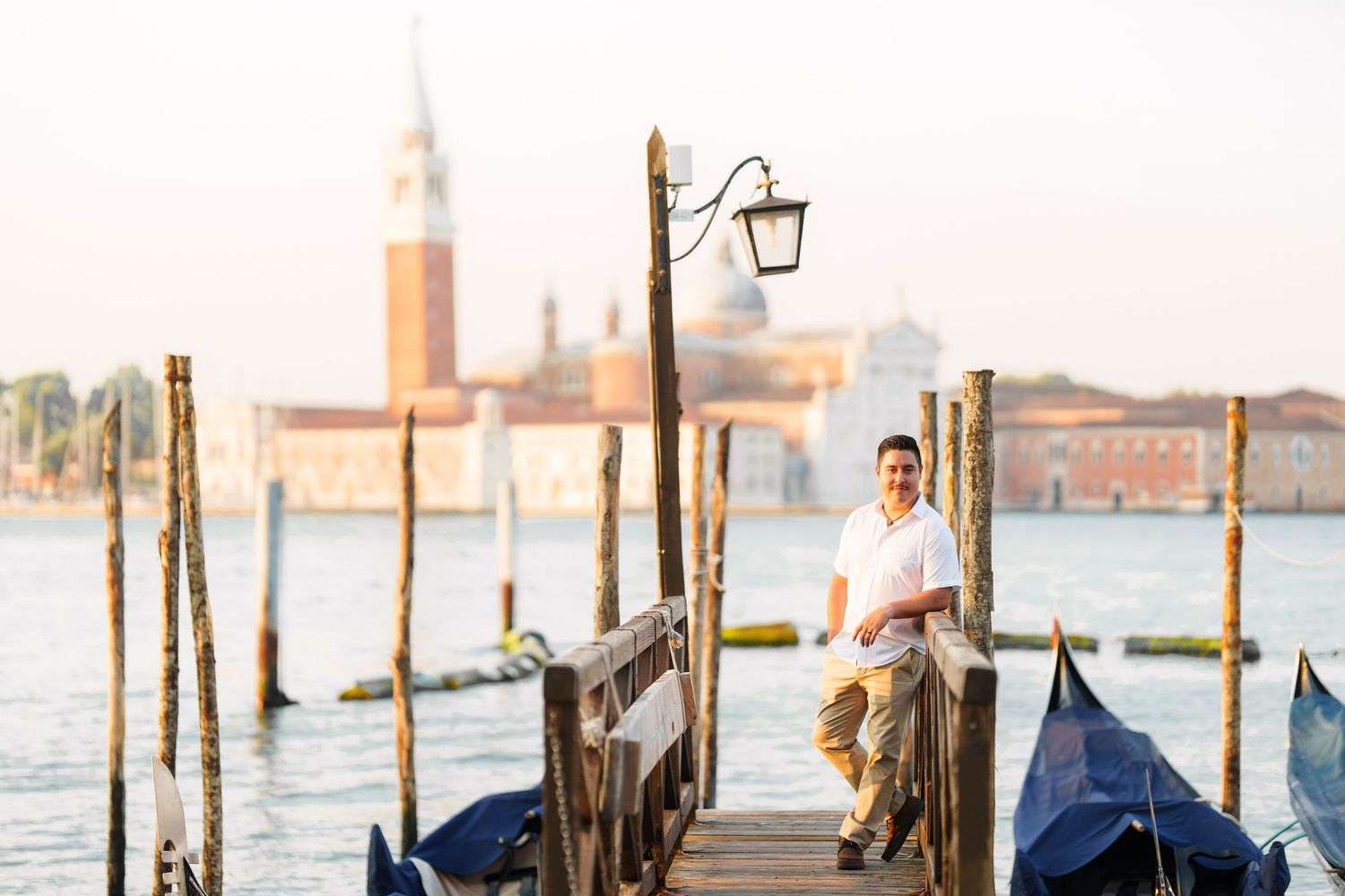 photographer veniceA scenic view of Venice's San Giorgio Maggiore with gondolas and wooden posts along the waterfront at sunset.