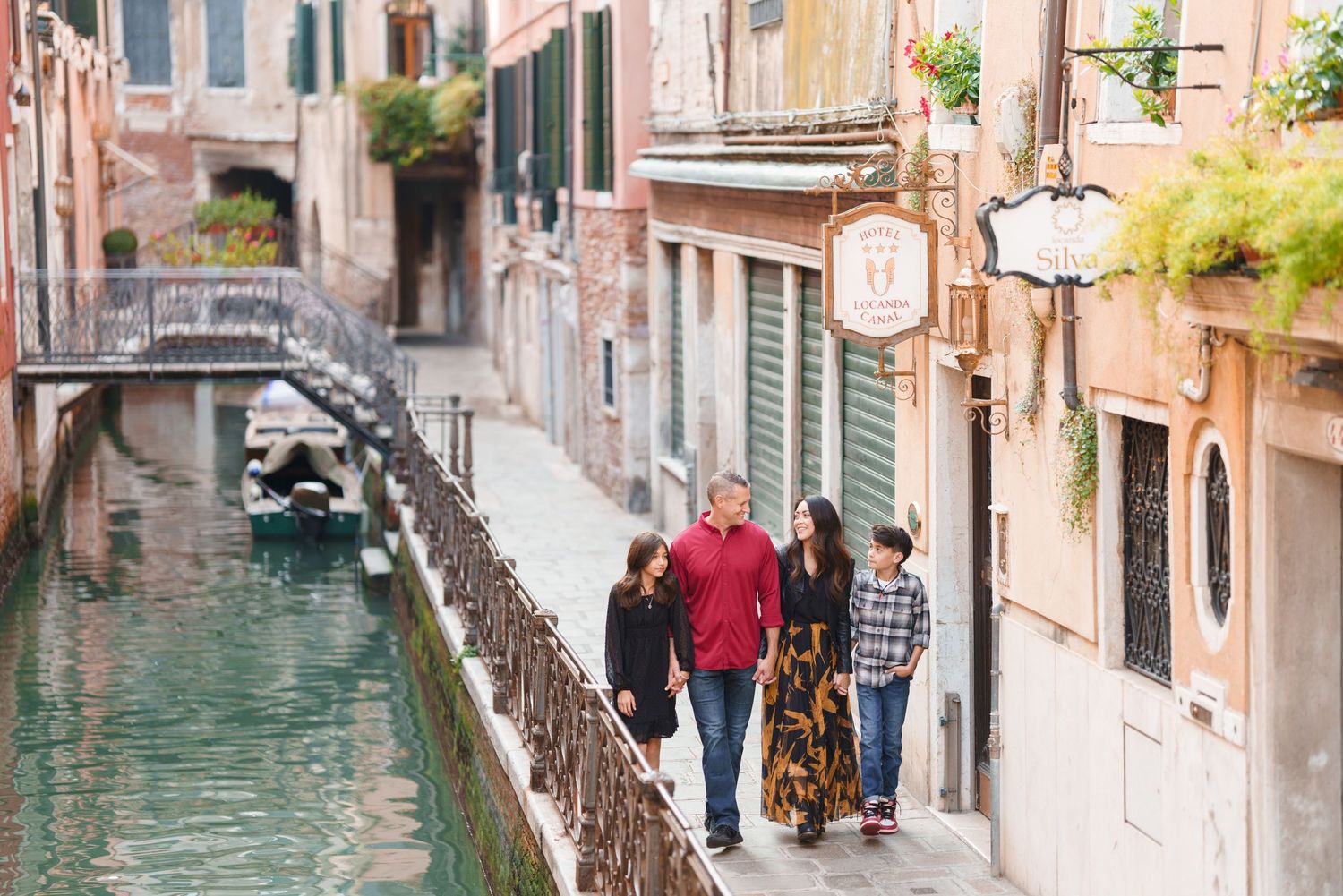 Narrow canal in Venice with traditional buildings, bridges, and colorful boats reflecting in turquoise water.