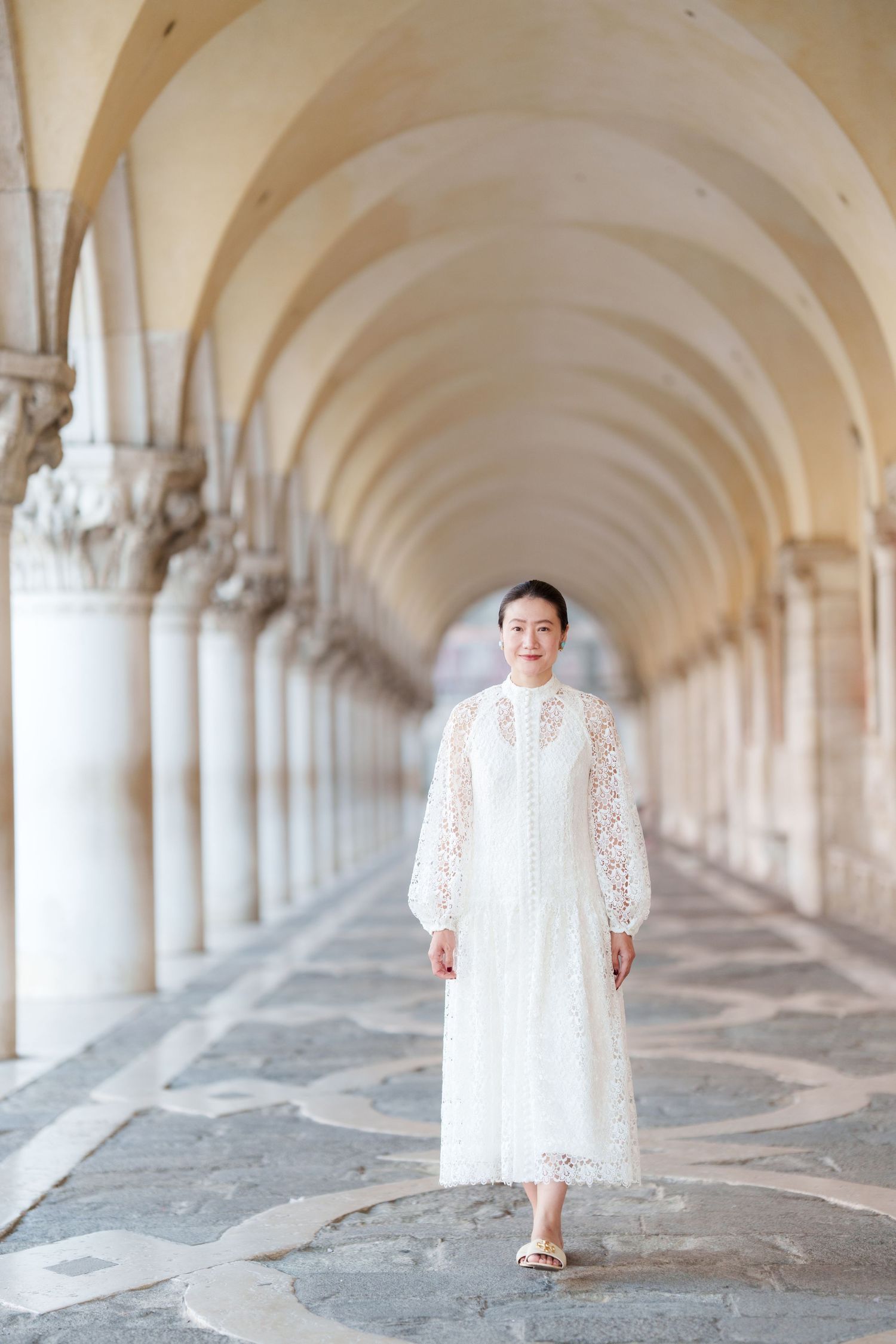 Woman in white lace dress posing under elegant arched colonnade in Venice, Italy.