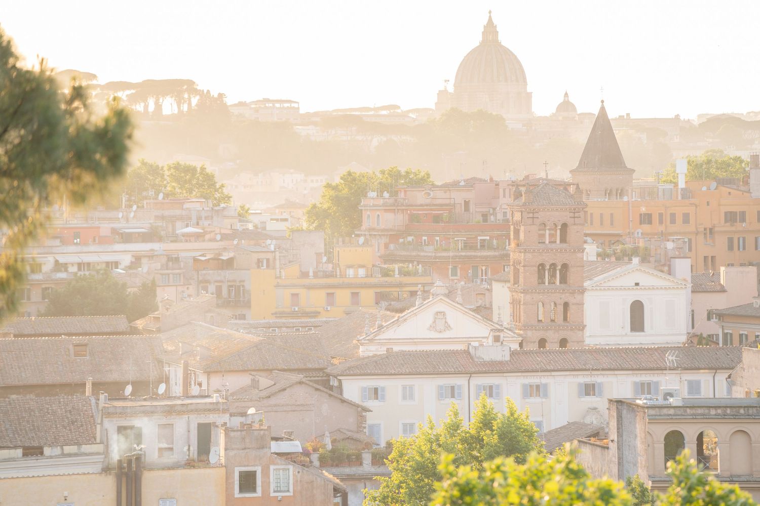 Golden hour sunlight bathes the historic rooftops and domes of Rome, Italy, in a warm, hazy glow.