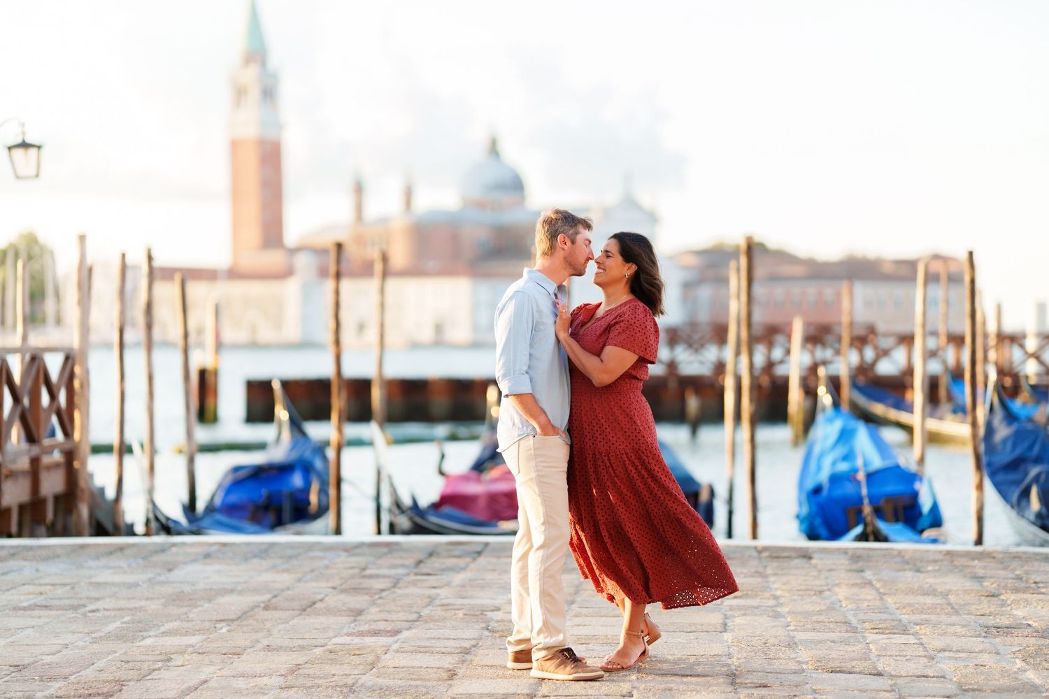 Romantic couple embracing on Venice waterfront with gondolas and San Giorgio Maggiore church in background.