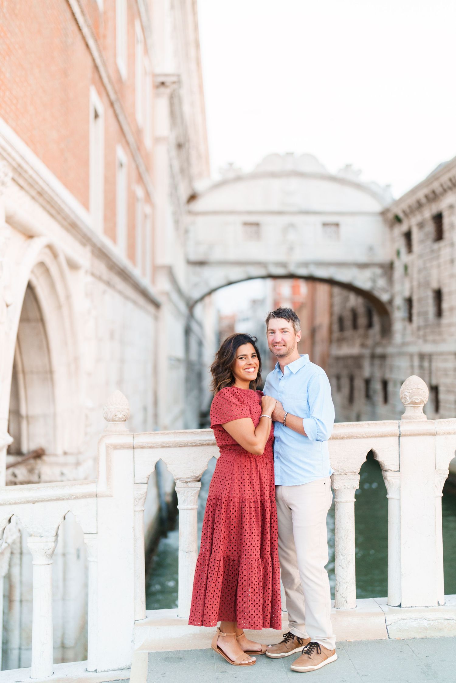 Couple posing on a bridge in Venice, Italy, with the Bridge of Sighs and canal in the background.