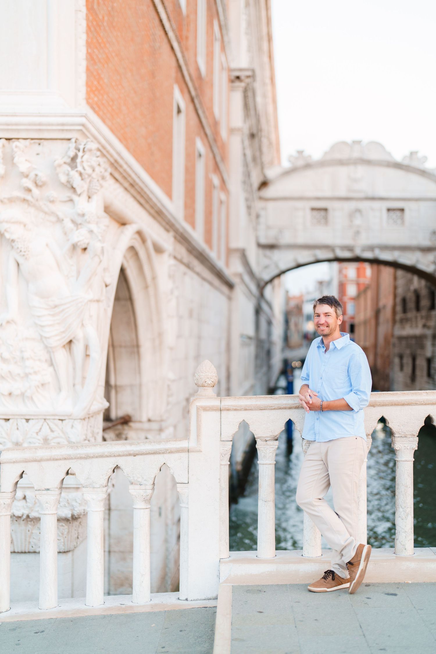 Man in blue shirt leaning on white marble railing near Bridge of Sighs in Venice, Italy.