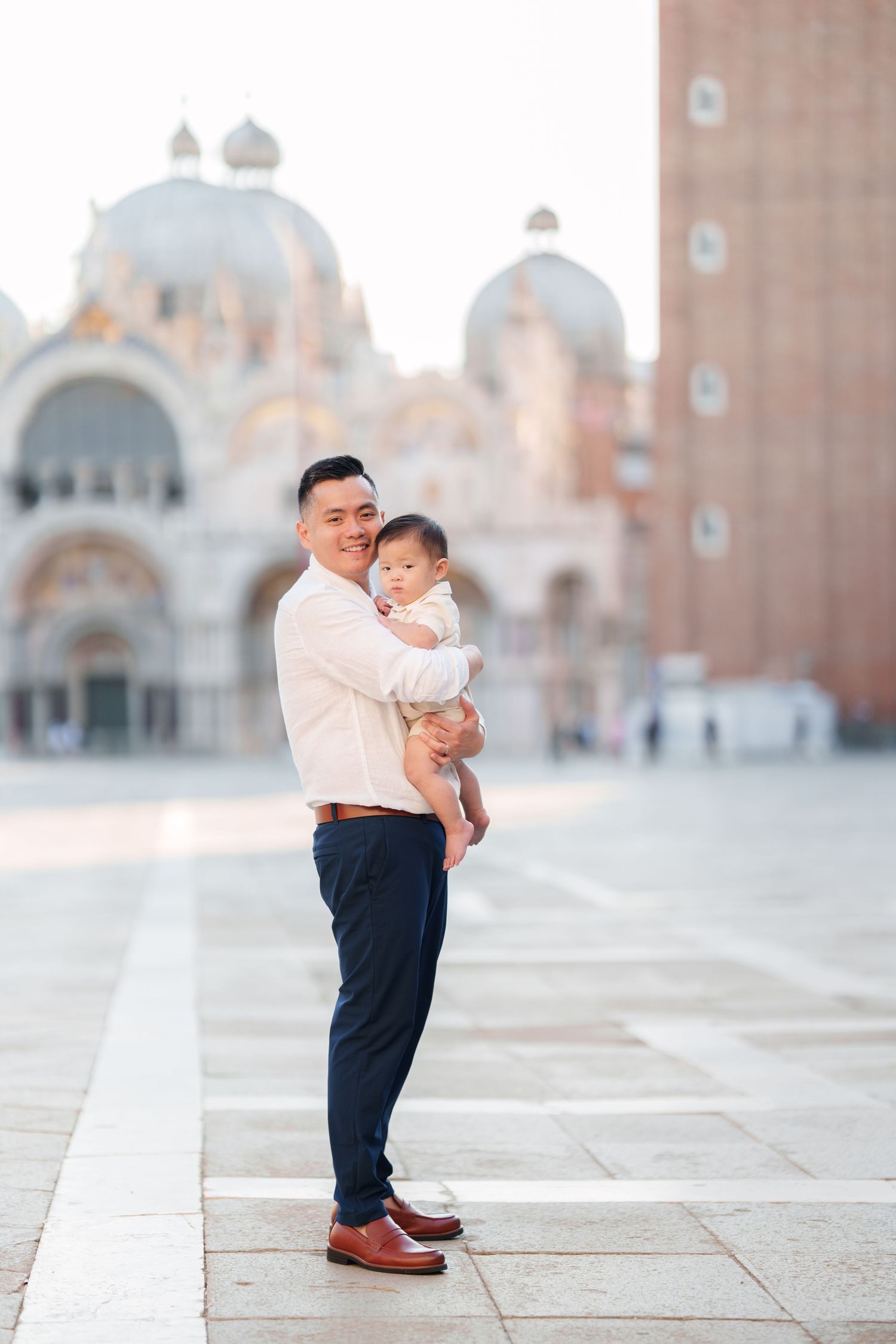 Father holding baby in Piazza San Marco, Venice, with St. Mark's Basilica in the background.