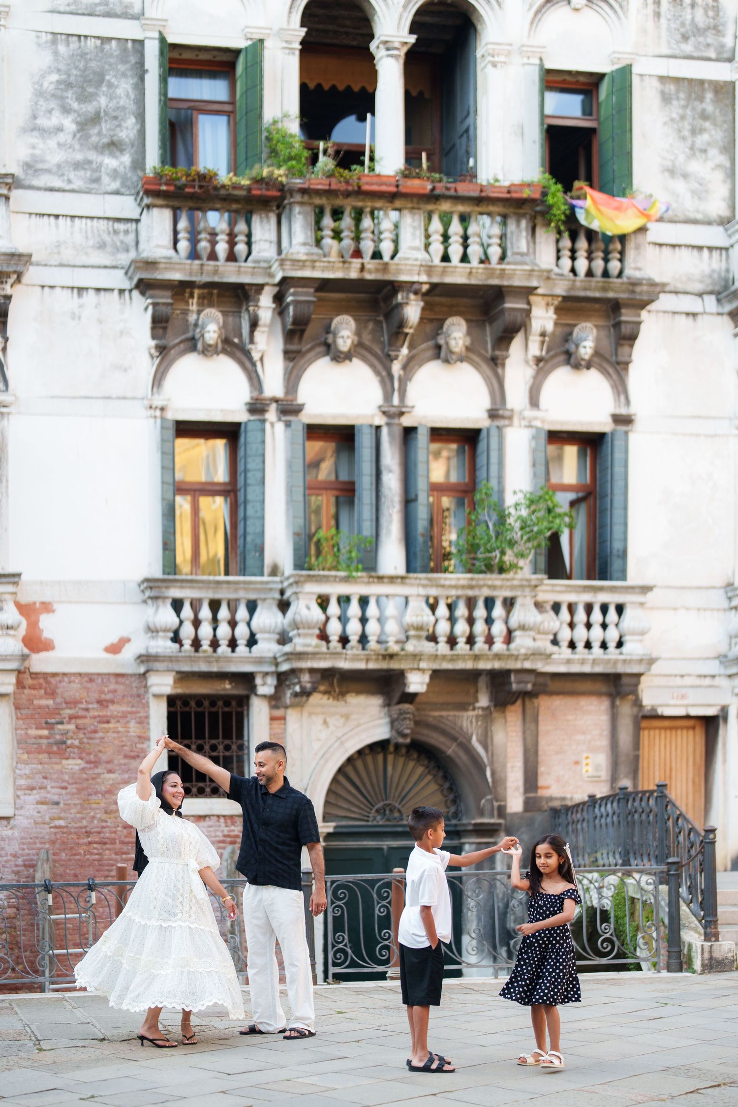 Family of four enjoying a sunny day in Venice, Italy, with historic architecture and balconies in the background.