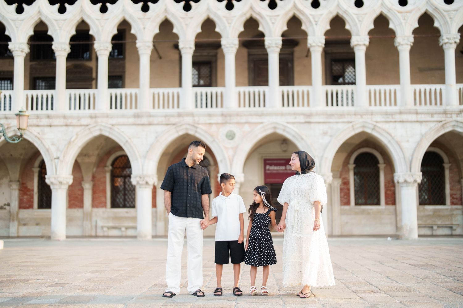 Family of four posing together at the ornate Doge's Palace arcade in Venice, Italy.