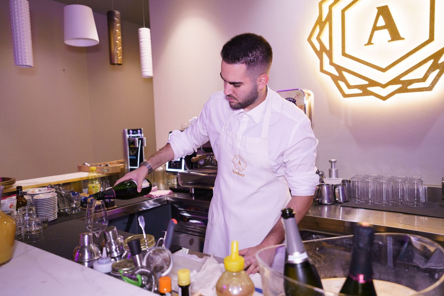 Bartender in white uniform pouring drinks at a stylish bar with champagne bottles and glassware.
