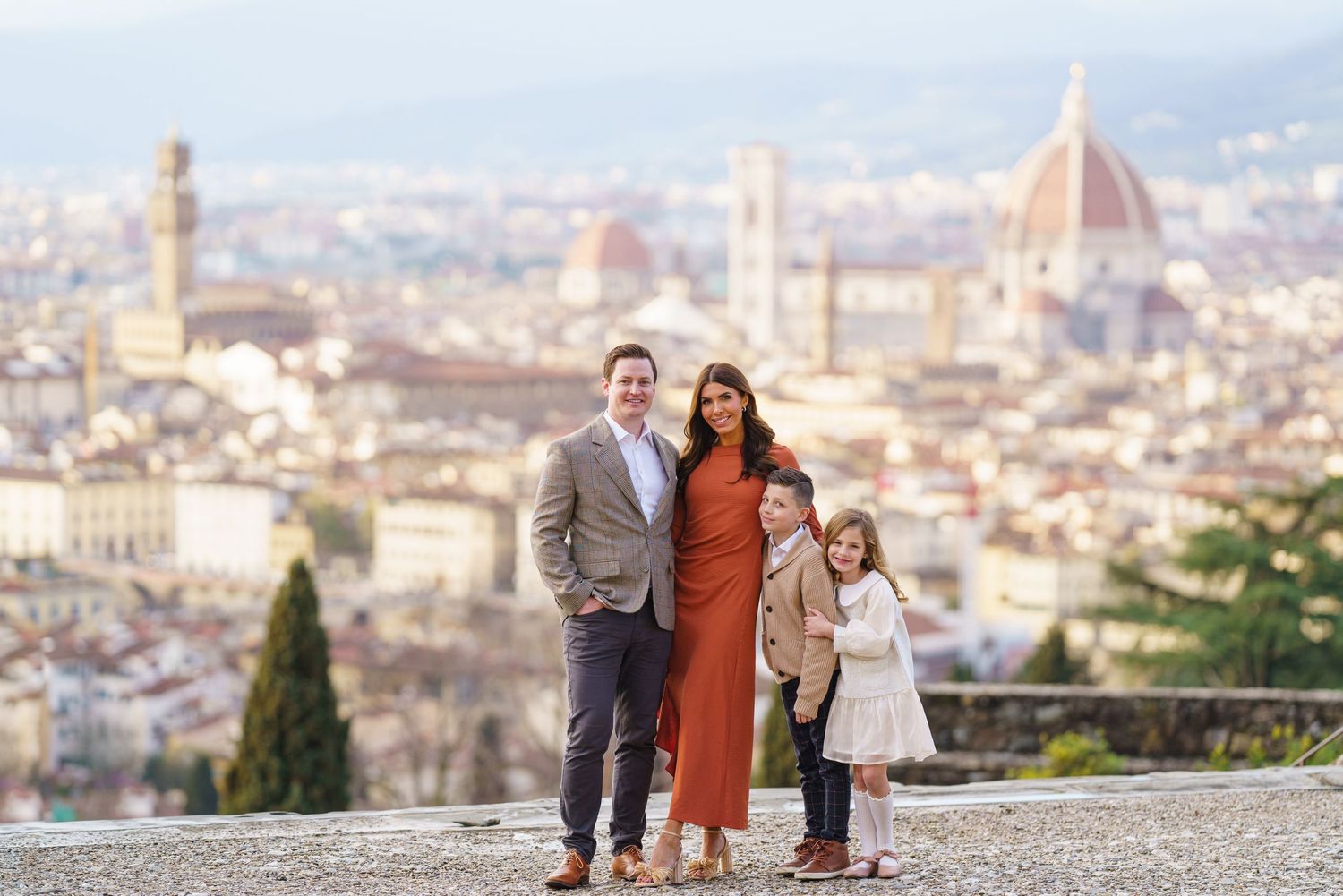 Family of four posing with Florence skyline featuring the Duomo cathedral in the background on a sunny day.