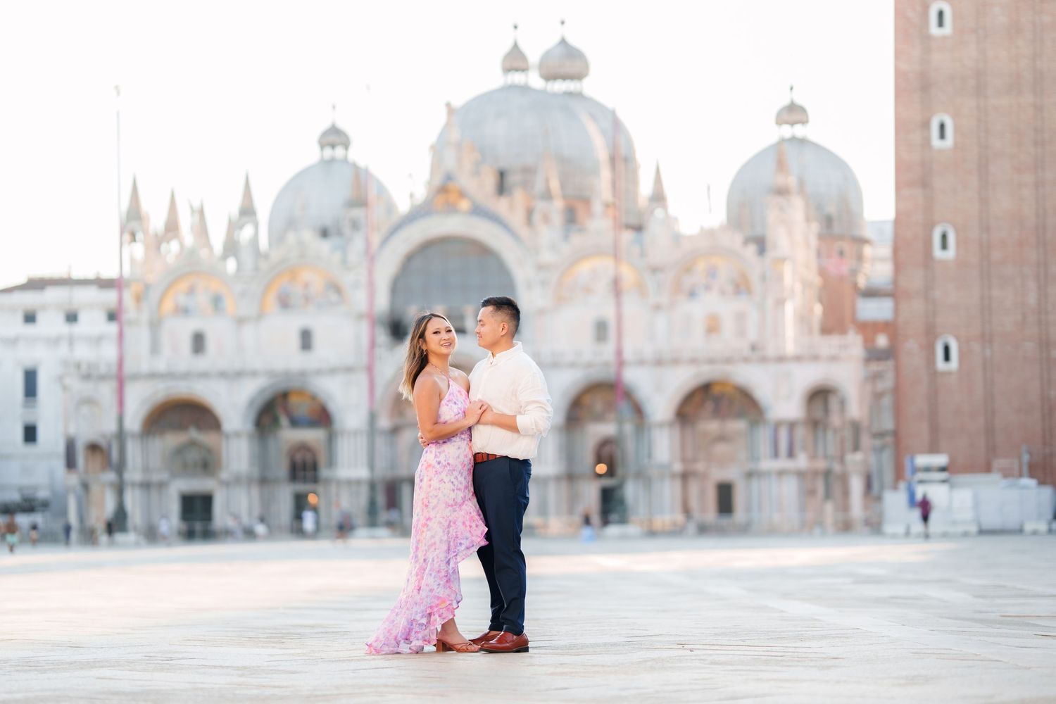 Couple embracing in St. Mark's Square, Venice, with the iconic Basilica di San Marco in the background at sunrise.