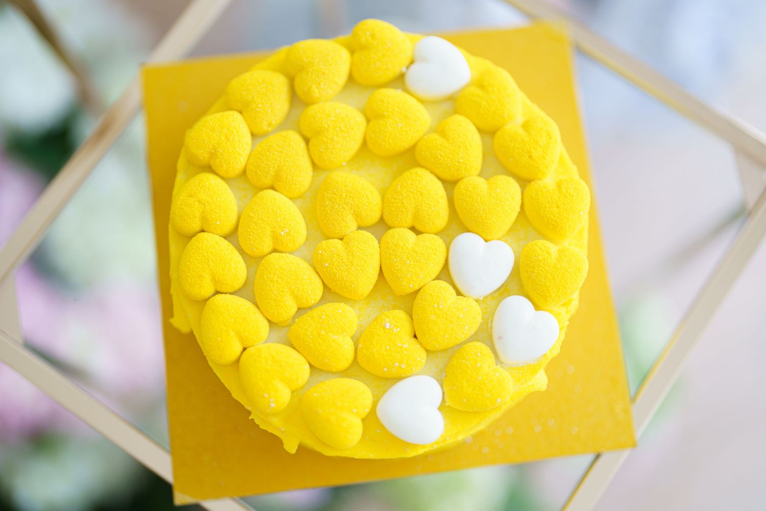 Yellow heart-shaped candy-covered round cake with white heart accents on a yellow board.