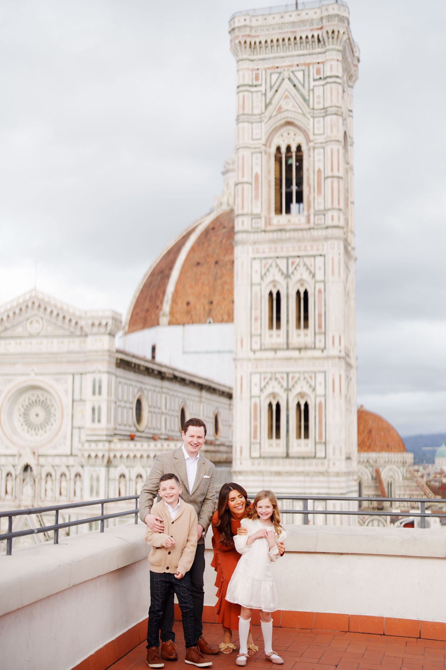 Family of four posing on a rooftop terrace with Florence Cathedral and Giotto's Campanile in the background.