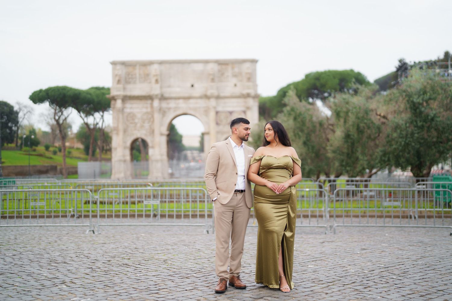 Couple in matching olive outfits posing before the Arch of Constantine in Rome during a maternity photoshoot.