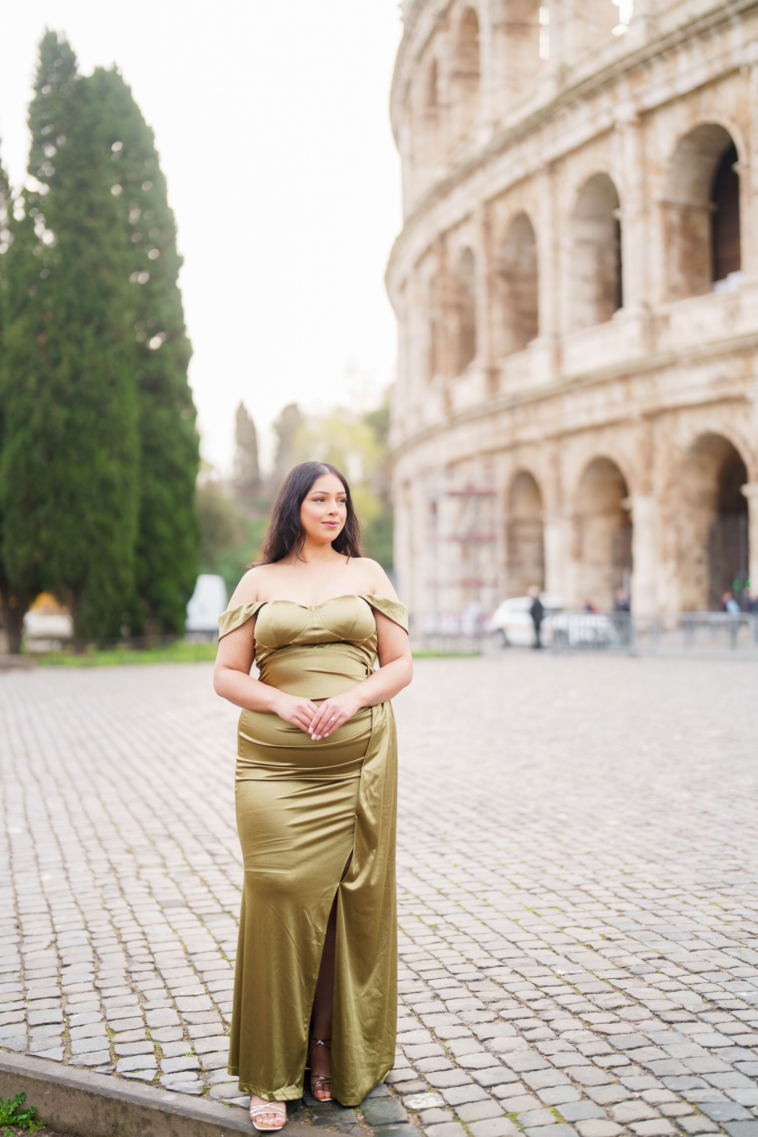 Pregnant woman in gold satin gown posing in front of the Colosseum in Rome, Italy.