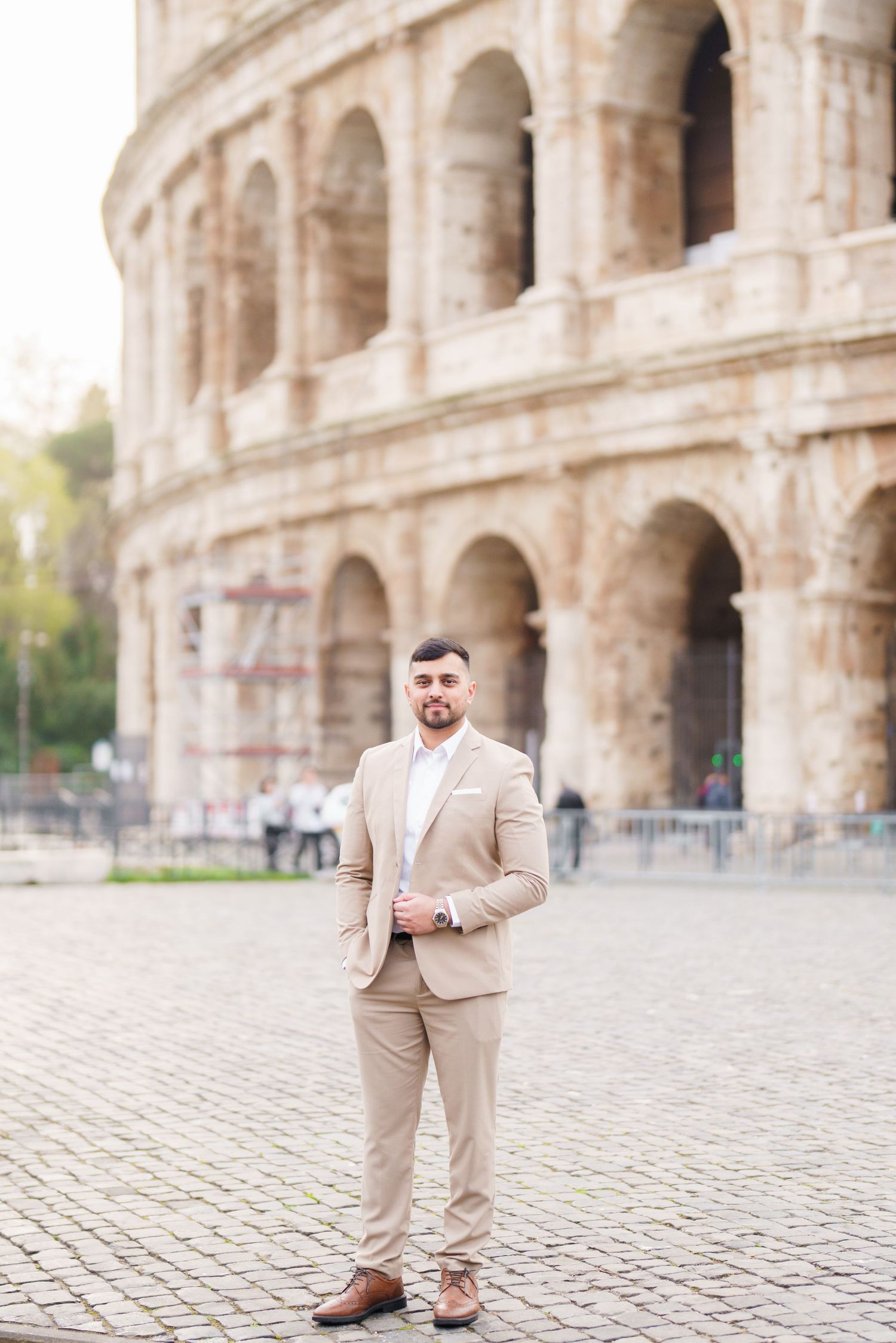 Man in beige suit posing confidently in front of the Colosseum in Rome, Italy.