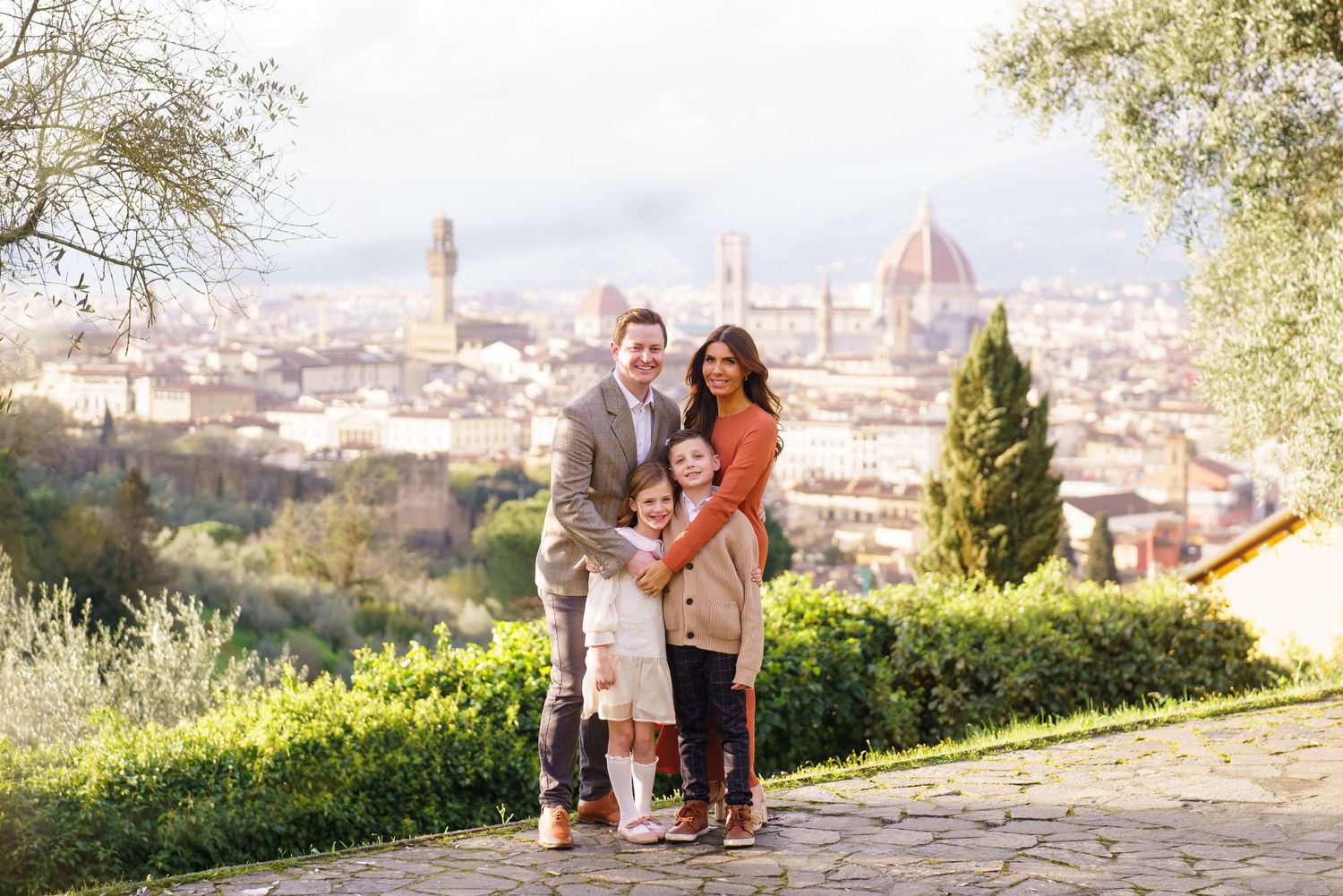 Family of four posing together on a scenic overlook with Florence Italy skyline and cathedral dome in background.