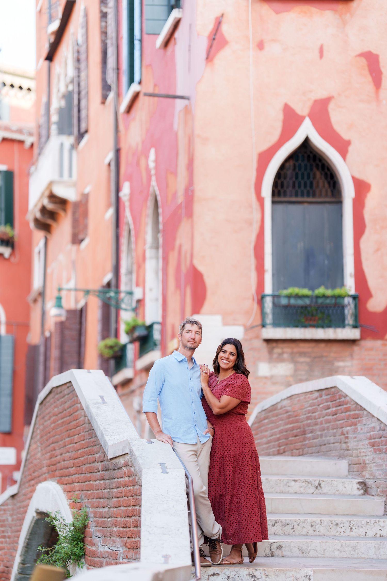 Couple posing on a brick bridge in Venice, Italy, surrounded by colorful historic buildings.