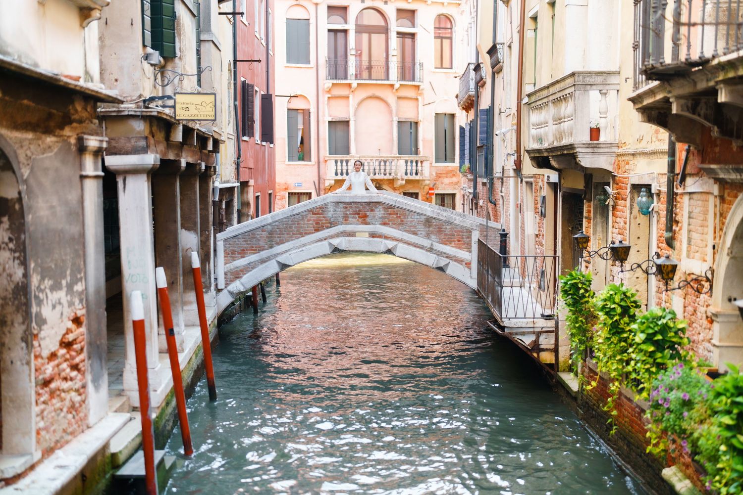A picturesque Venice canal with a small stone bridge connecting historic brick buildings on a calm waterway.