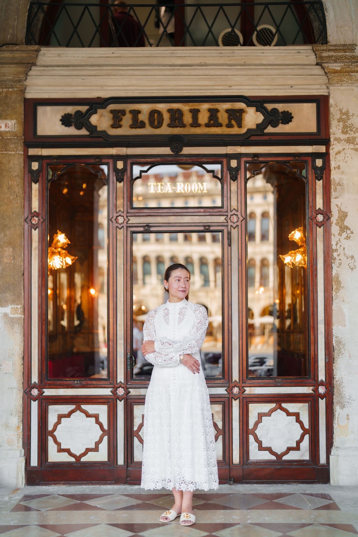 Woman in white lace dress standing before Cafe Florian Tea Room entrance in Venice, Italy.