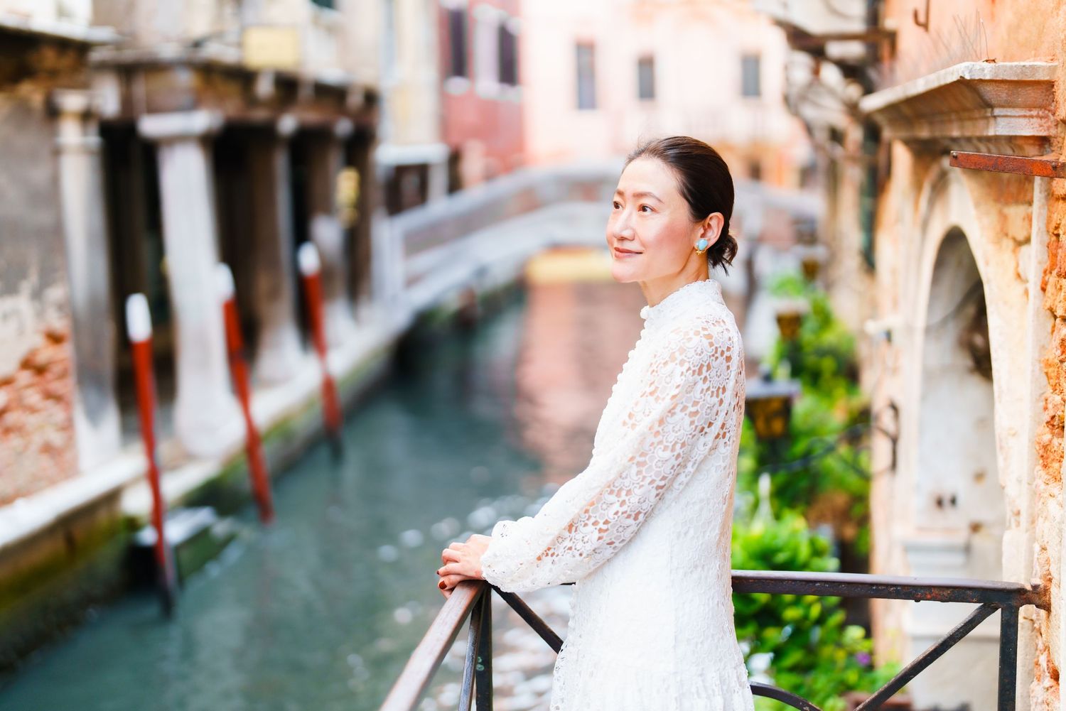 Woman in white lace dress posing on a bridge over a Venice canal with historic architecture in the background.