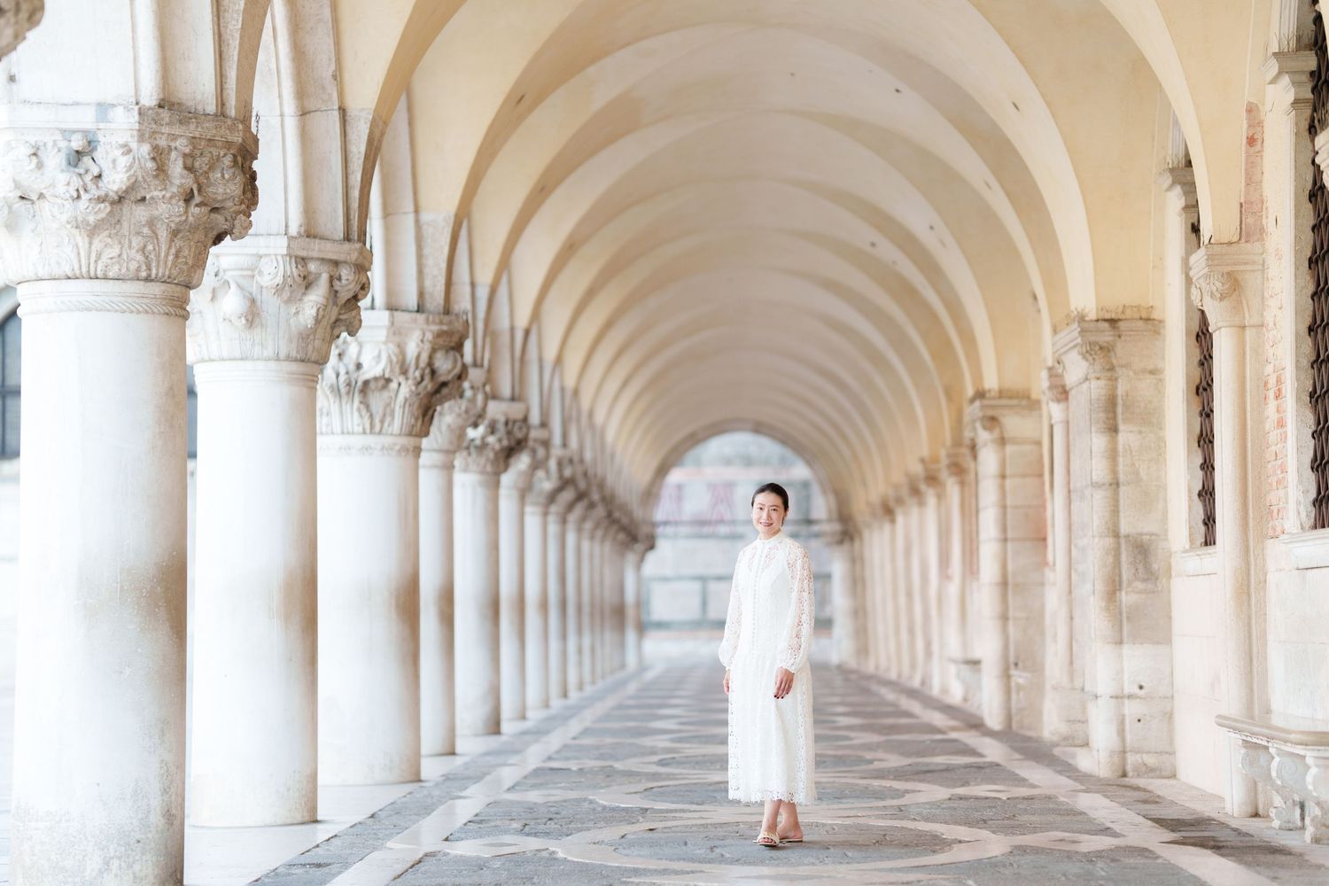 Woman in white dress posing under elegant arched colonnade in Venice, Italy.