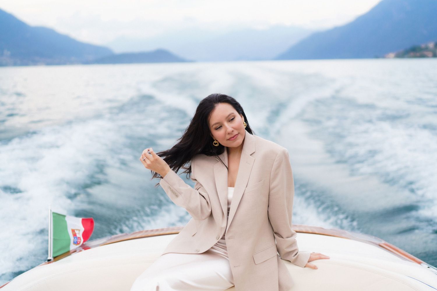A person in beige outfit lounges on a white boat deck while cruising across blue ocean waters on a sunny day.