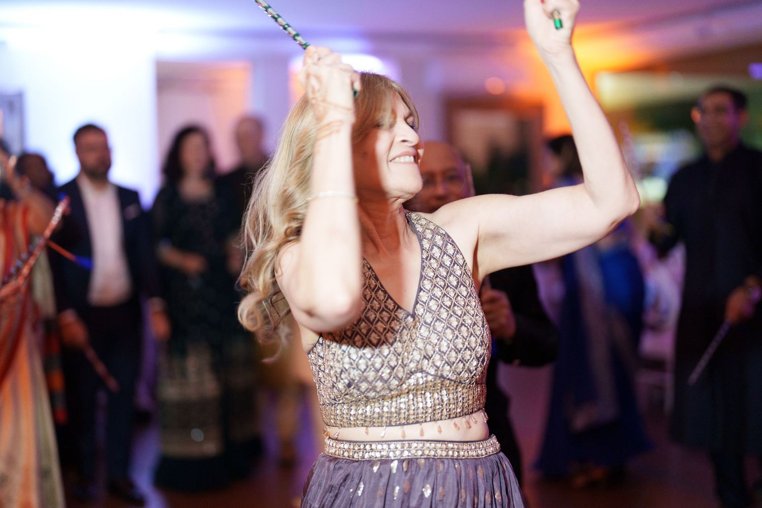 Guest in sparkly dress raises sparklers while dancing at an indoor celebration.