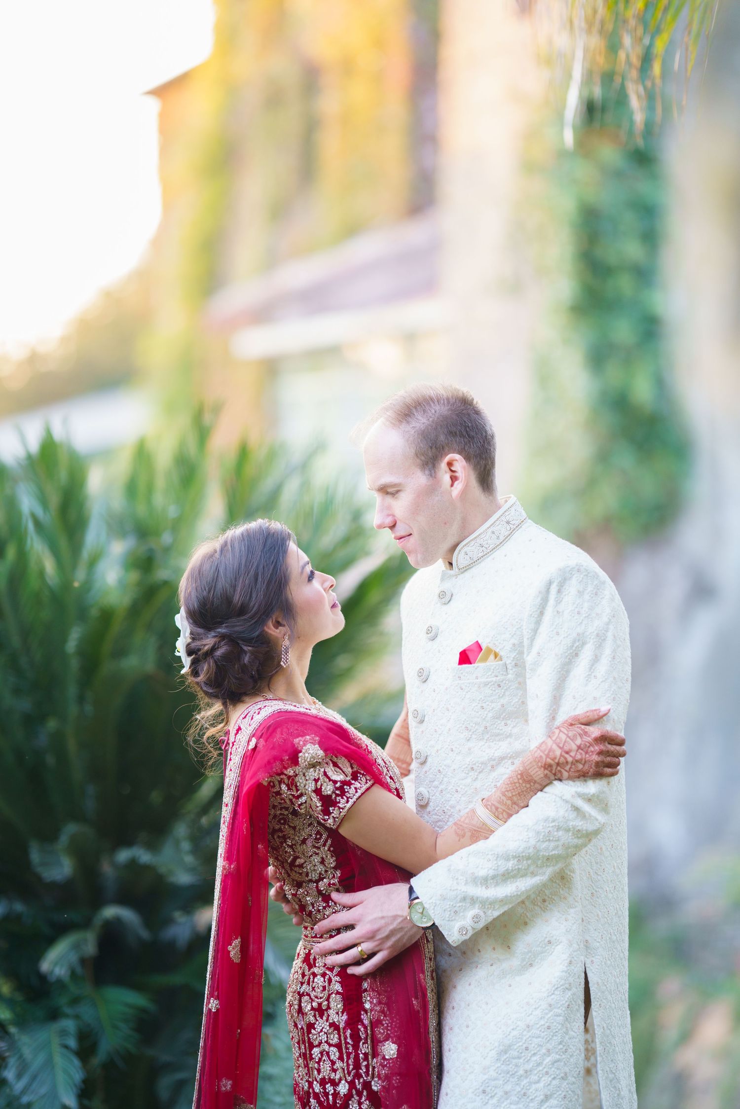 A tender moment between newlyweds in traditional fusion wedding attire against an ivy-covered building.