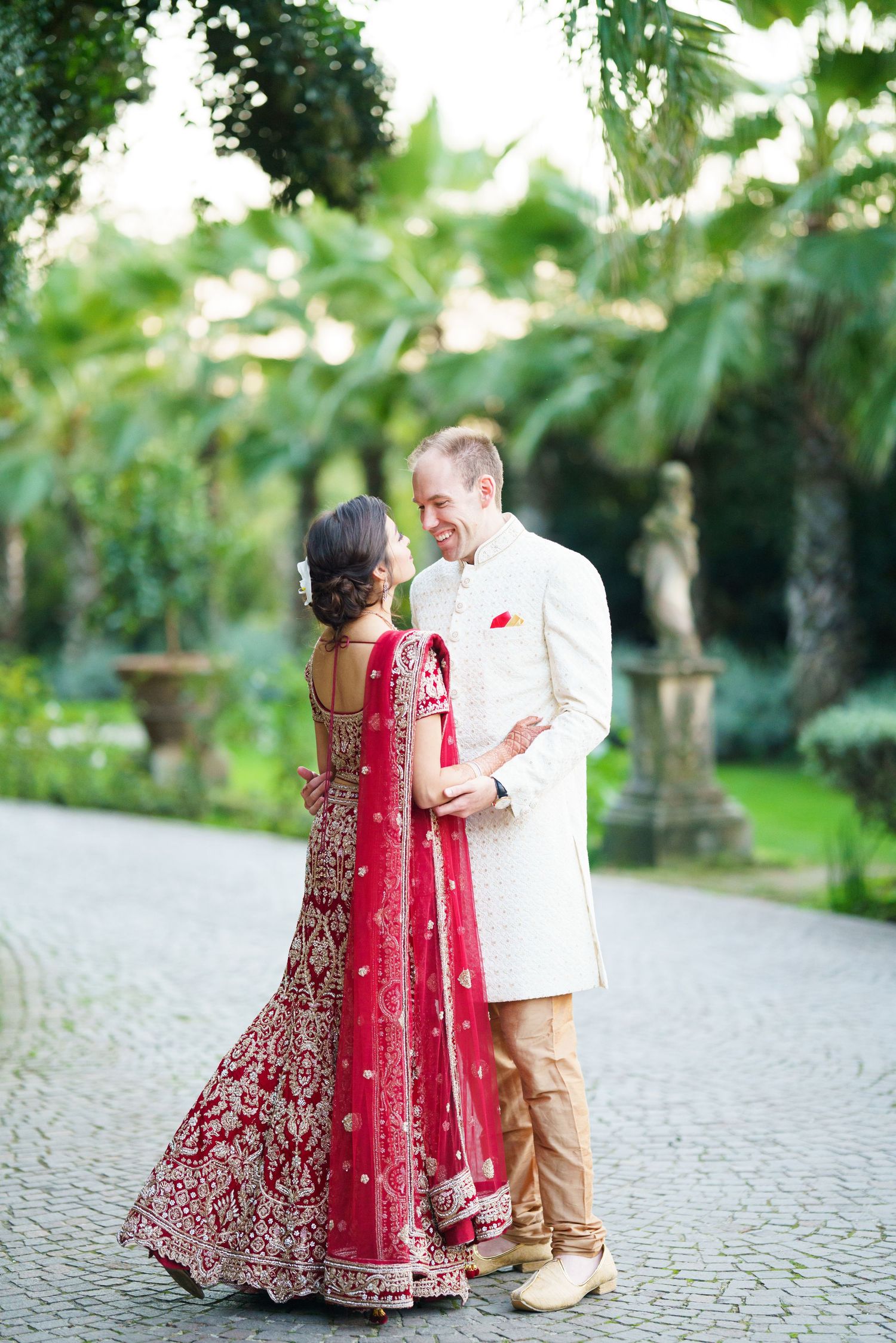 A couple dances together on a stone path, with the bride wearing a red embroidered lehenga.