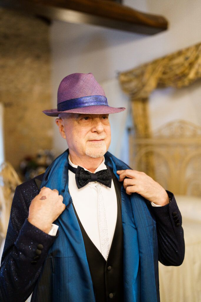 Man in formal navy suit and hat adjusting his bowtie in sequential shots.