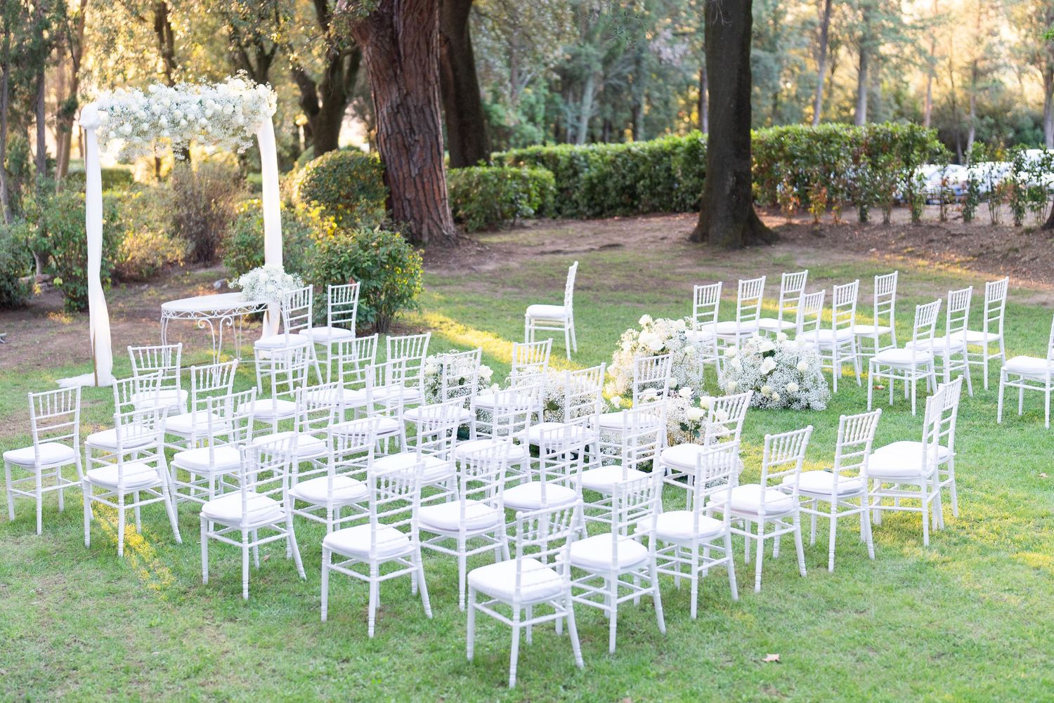 White chairs arranged in rows on a grassy lawn for an outdoor wedding ceremony.