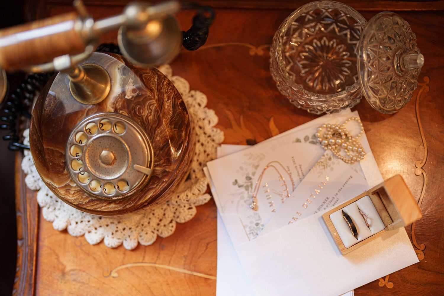 Vintage crystal decanter and wedding details arranged on wooden surface.