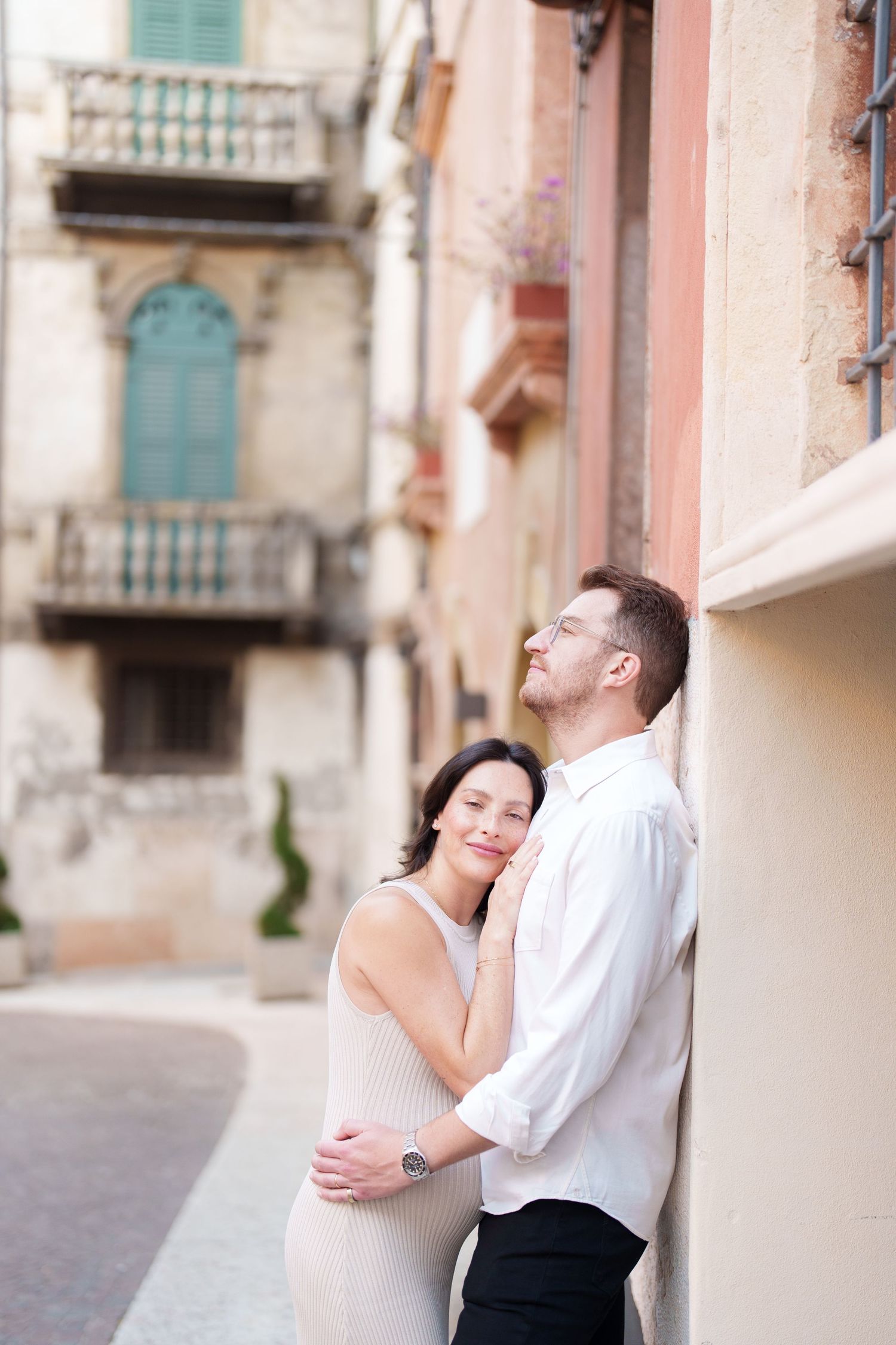 A romantic couple embraces against a pastel Mediterranean building wall with vintage architectural details.